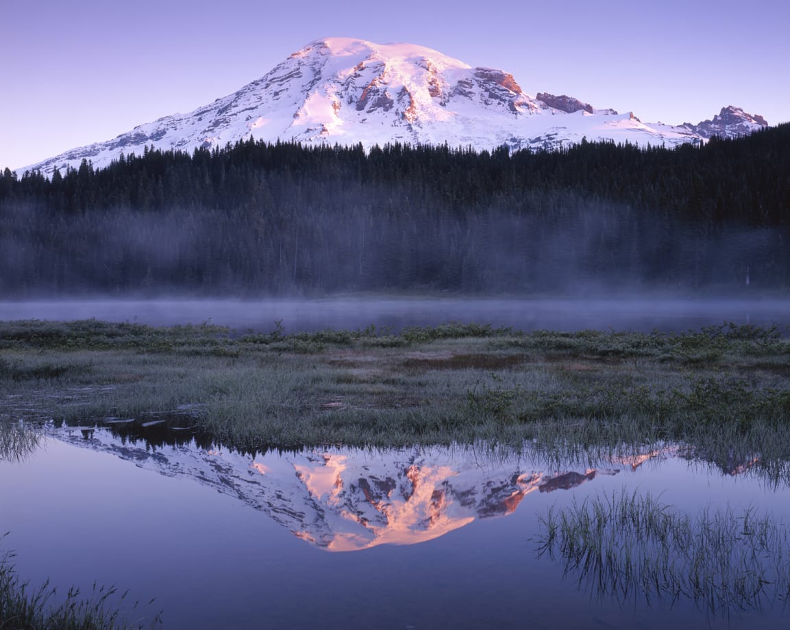 A mountain with snow on top and trees in the background.