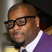 A man in glasses and purple jacket standing next to stairs.